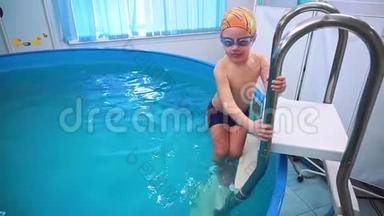 一个小男孩爬上游泳池的楼梯，跳进水里。